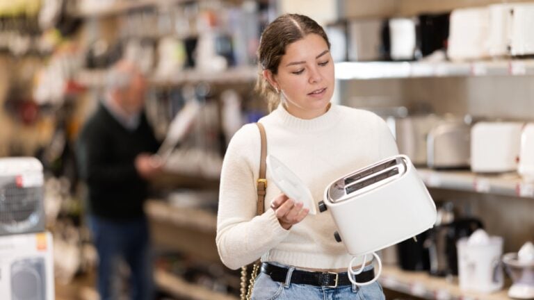 Young woman buyer chooses electric toaster in home appliance store