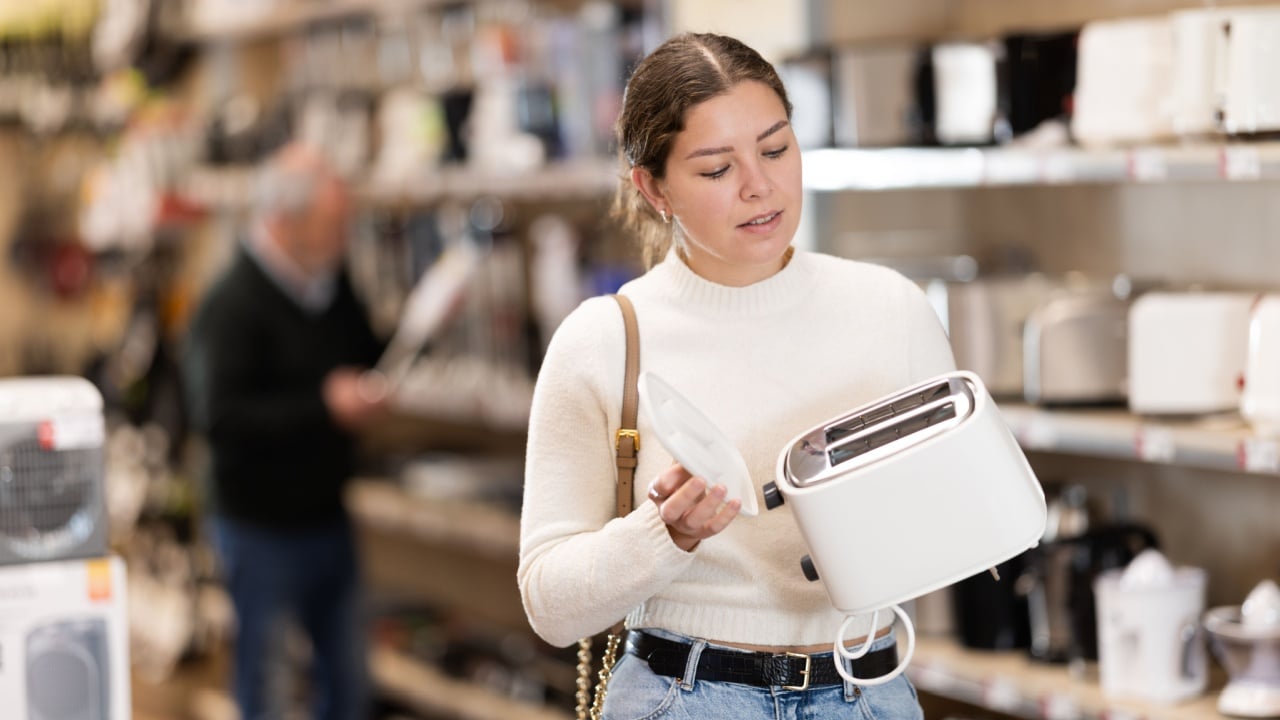 Young woman buyer chooses electric toaster in home appliance store