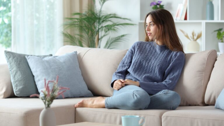 Pensive woman in blue looking at side sitting on a couch at home