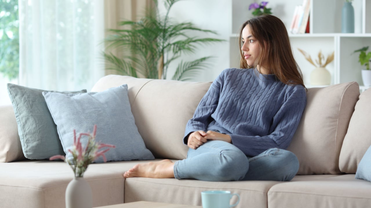 Pensive woman in blue looking at side sitting on a couch at home