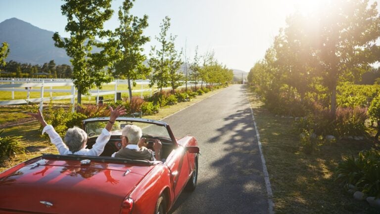 Elderly couple, car drive or road trip with sunshine for romantic getaway, adventure or journey. Senior, man and woman with vehicle on street for holiday, travel or outdoor vacation in countryside