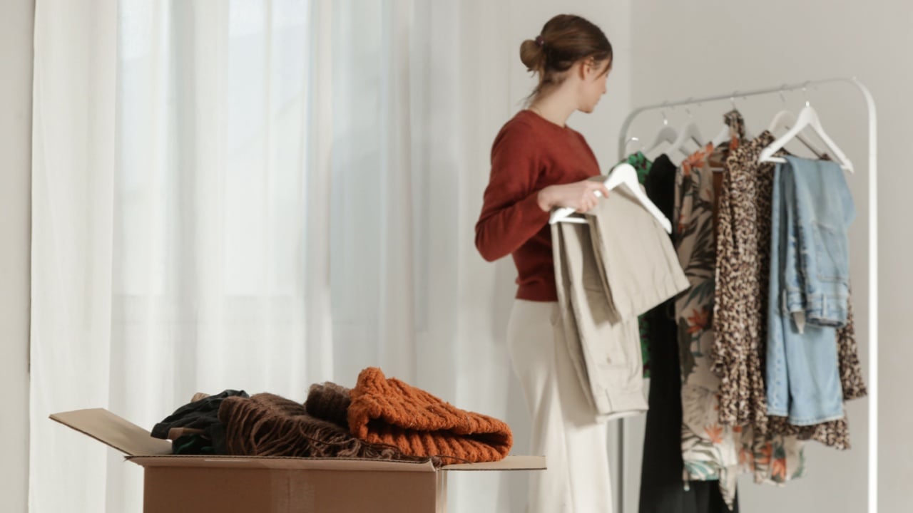 Spring Cleaning Organization, Decluttering, Moving and Donation Concept – Woman Sorting and Packing Clothes into Cardboard Box at Home