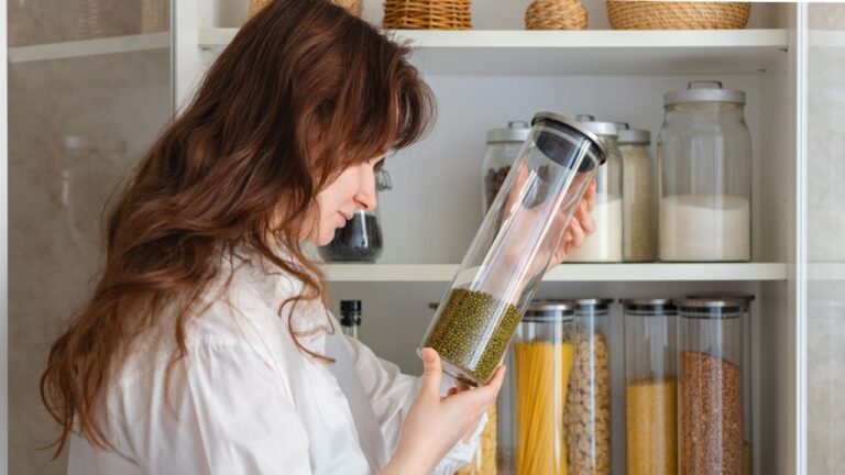 Young woman taking jar of legumes, lentils from shelf in kitchen, vegetarianism, healthy eating