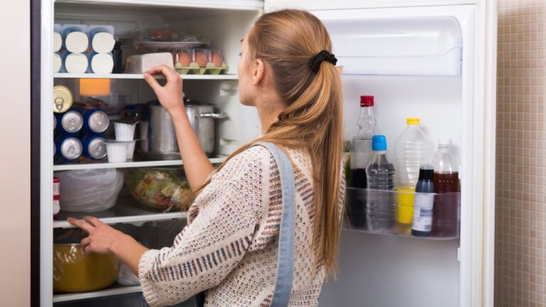 Young housewife arranging products on fridge shelves