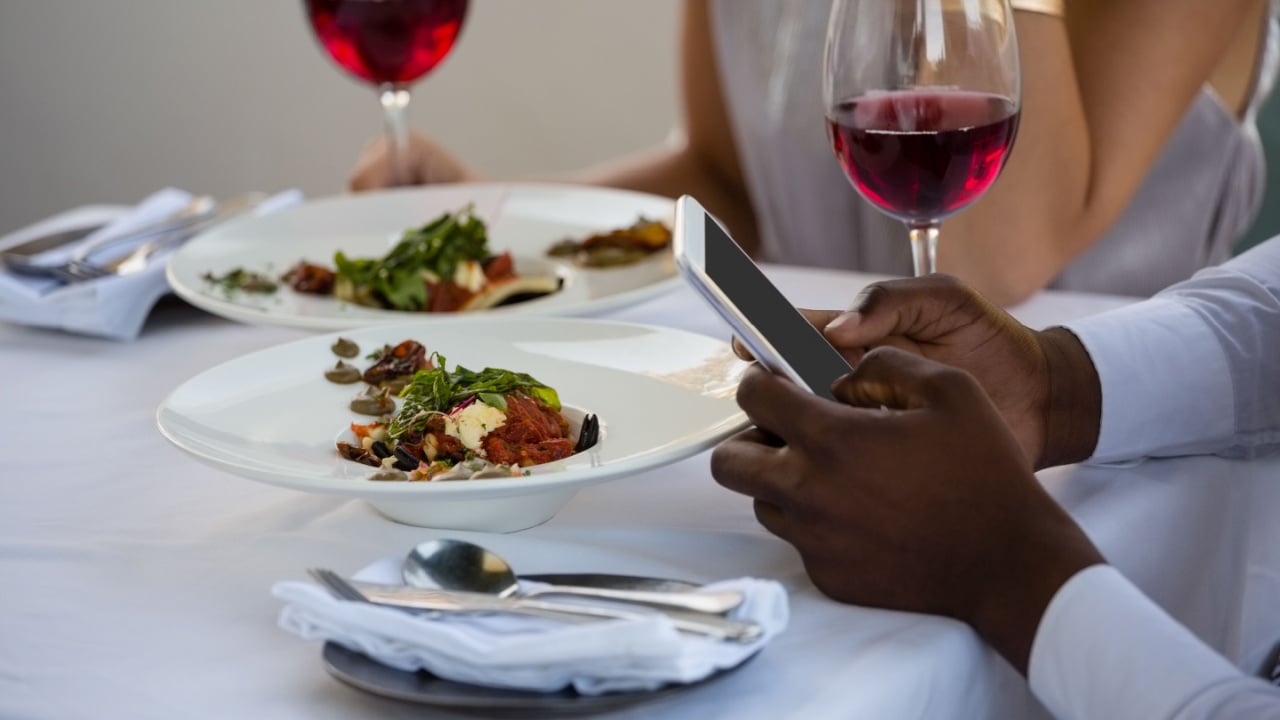 Cropped hands of man using mobile phone while sitting by woman at table in restaurant
