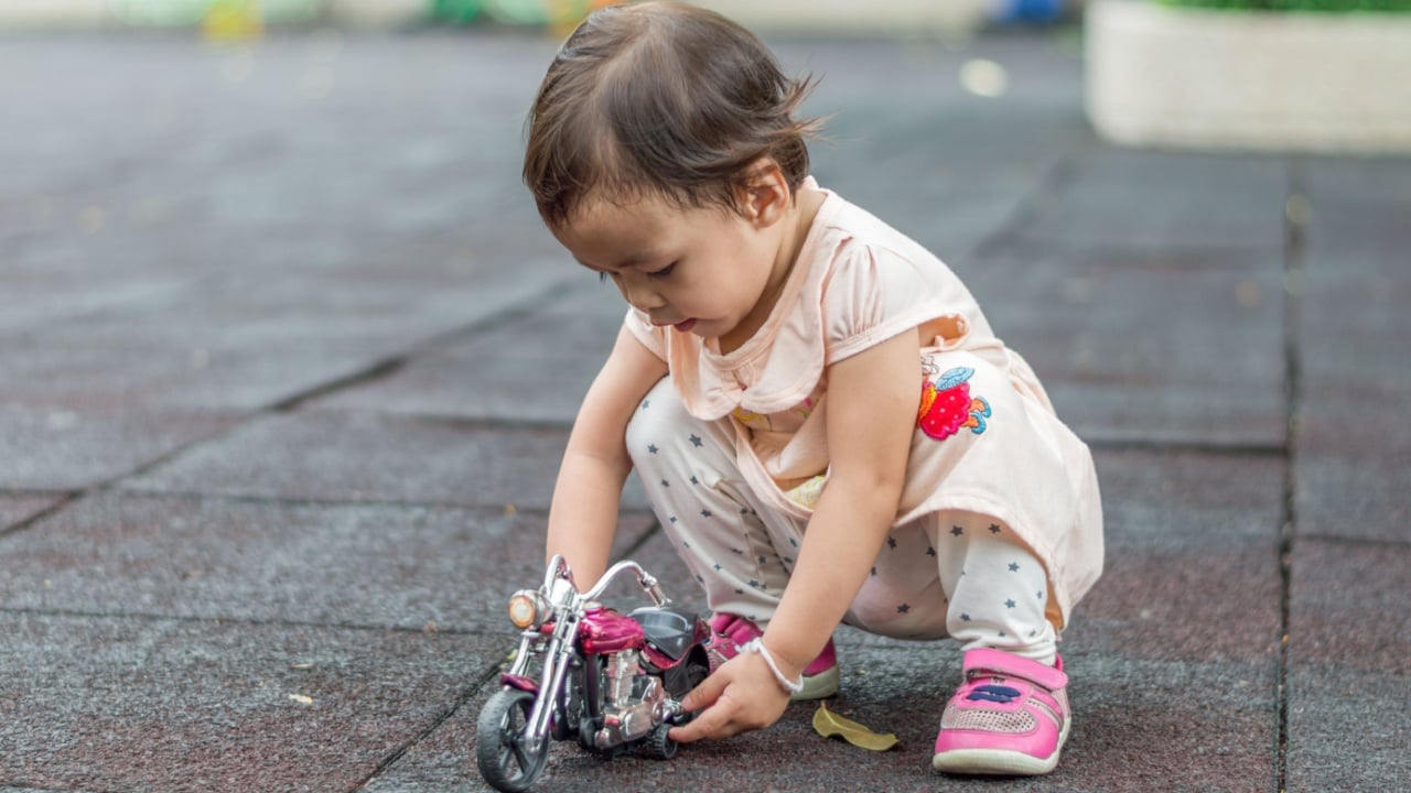 Asian baby girl playing bike toy on floor in playground.