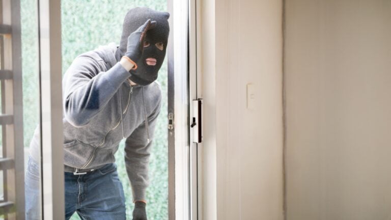 Suspicious man wearing a ski mask and carrying a plank looking through a glass door