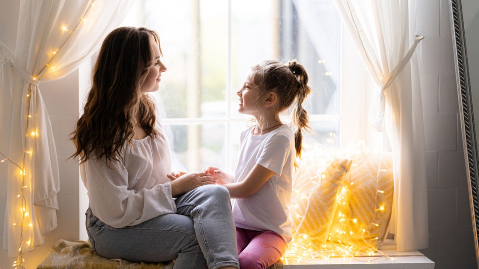 Unity mother and daughter concept. Girl hugging her mother, sitting on the window, showing her love at home