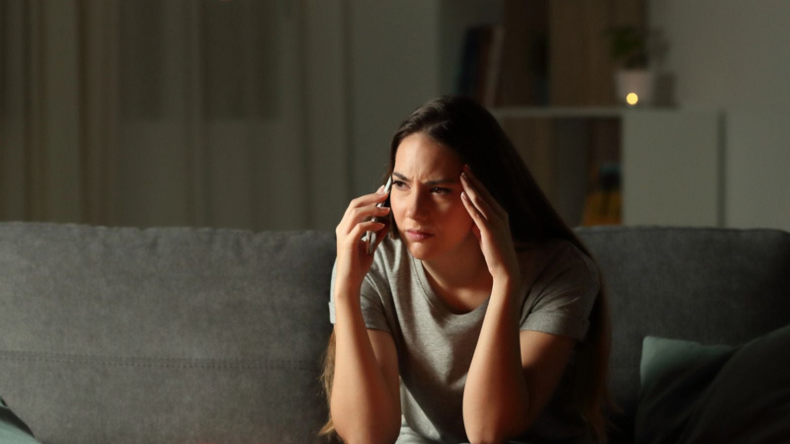 Worried woman talking on phone sitting on a couch waiting in the living room at home