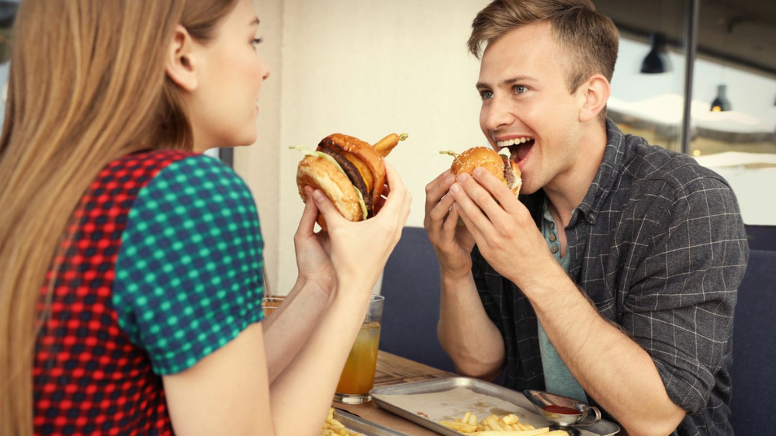 Young couple eating burgers in street cafe