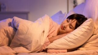 Young woman sleeping under blanket in bedroom at night