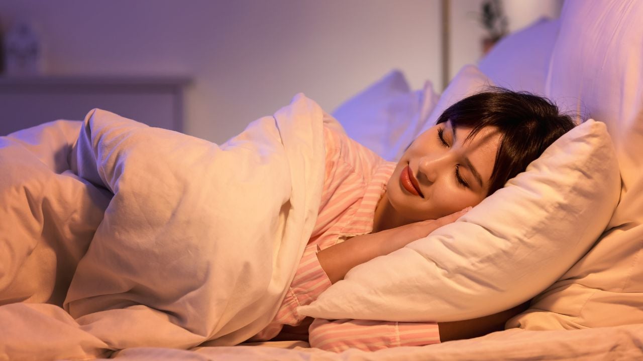 Young woman sleeping under blanket in bedroom at night
