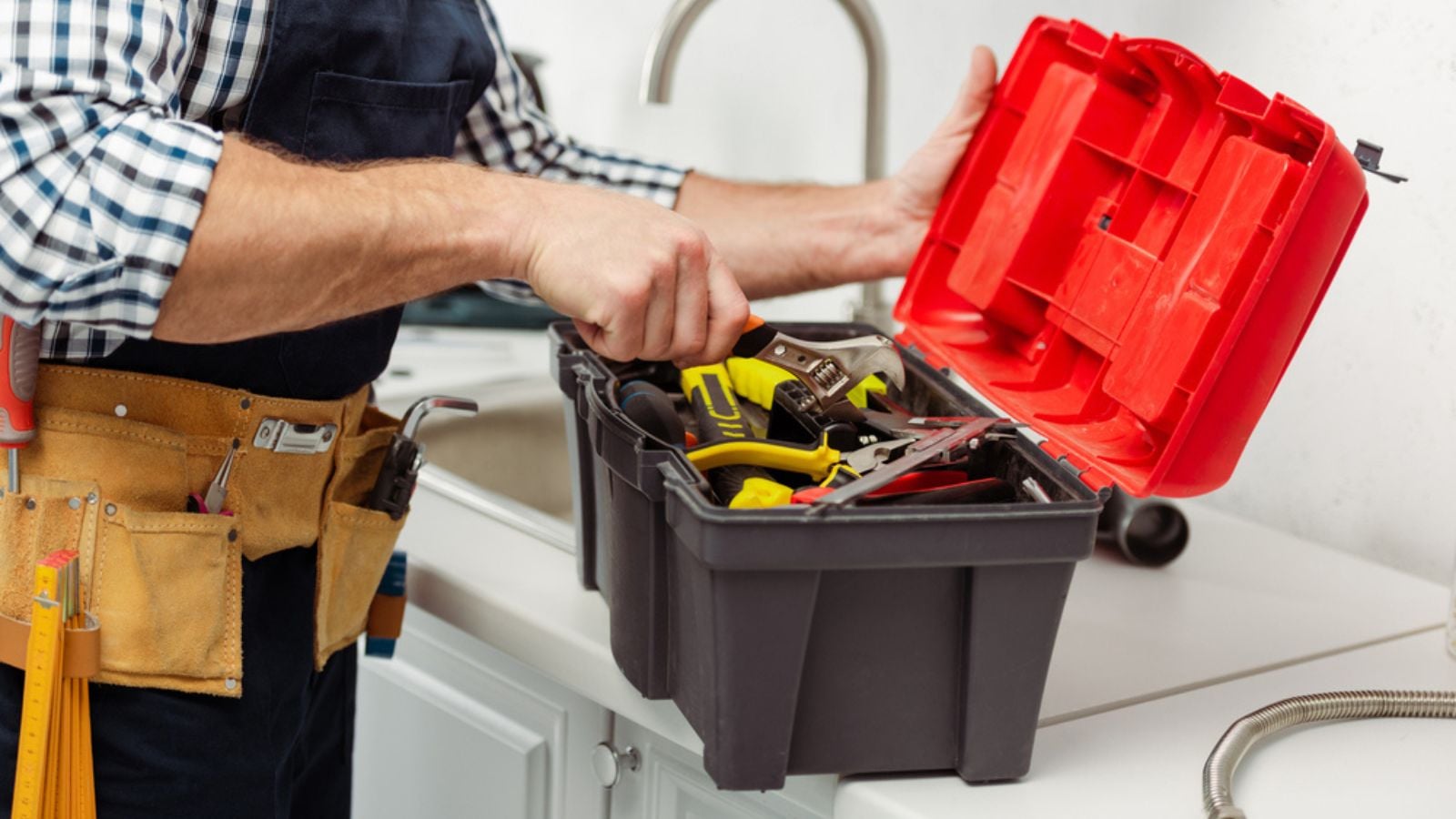 Cropped view of workman in overalls opening toolbox on kitchen worktop