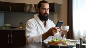 Male in a bathrobe sits at a table with a phone and breakfast