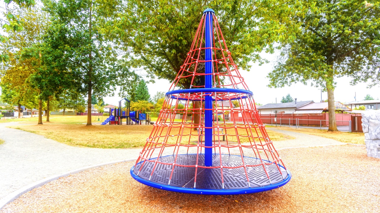 children's playground in the city park with a pyramid carousel, a hill in the form of a house, trees and houses in the background