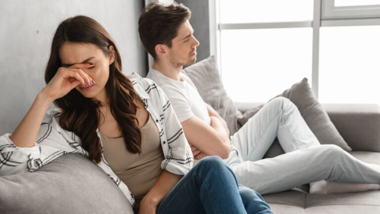 Photo of disappointed couple sitting together on sofa at home with upset look and expressing quarrel isolated over