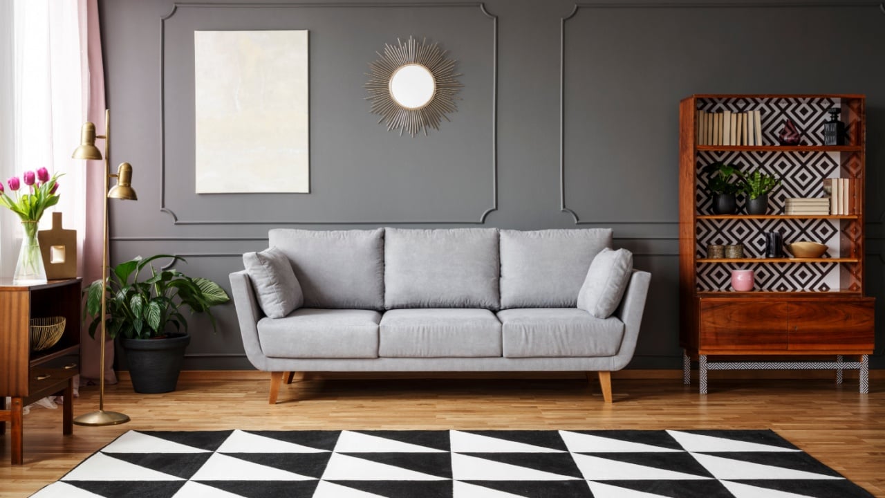 Black and white carpet with geometric pattern placed on the floor in dark living room interior with grey couch, vintage cupboard with books and wainscoting on the wall