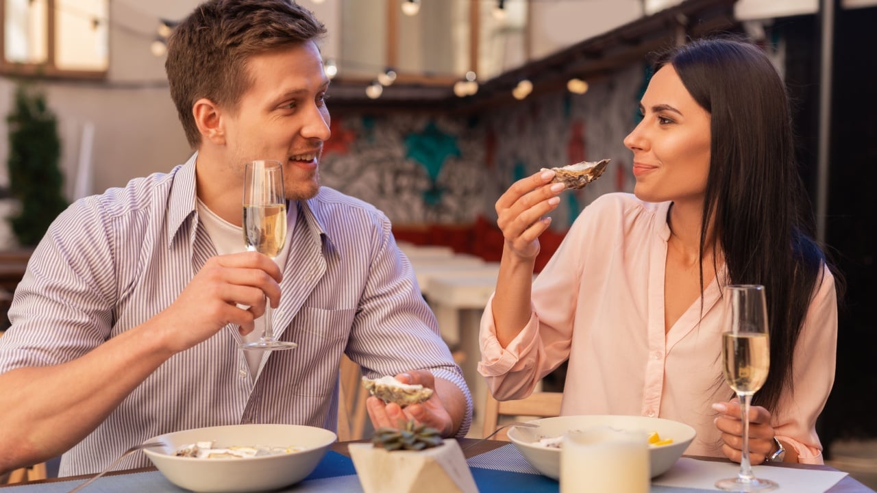Blonde-haired man. Blonde-haired elegant man inviting her appealing woman for drinking champagne and eating oysters