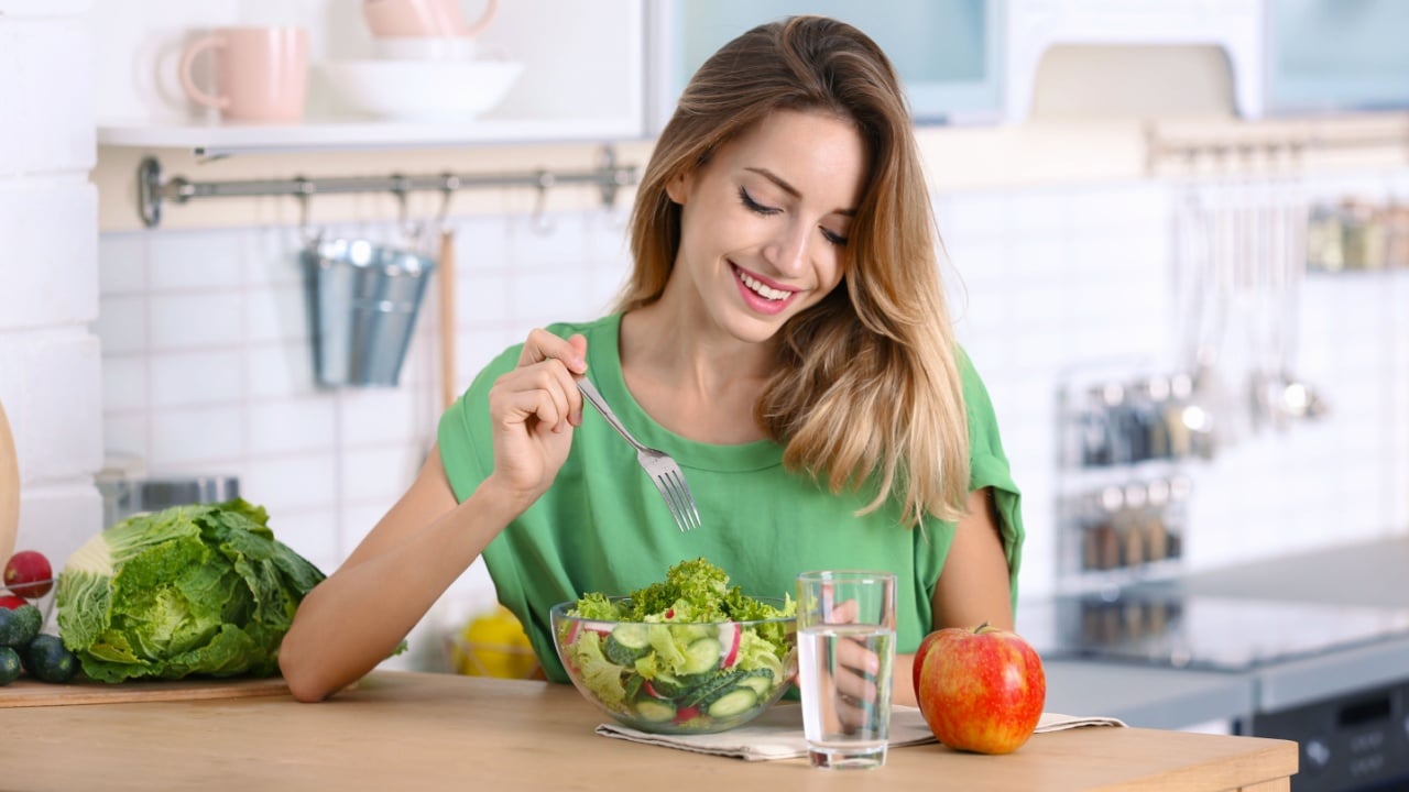 Woman eating vegetable salad at table in kitchen. Healthy diet