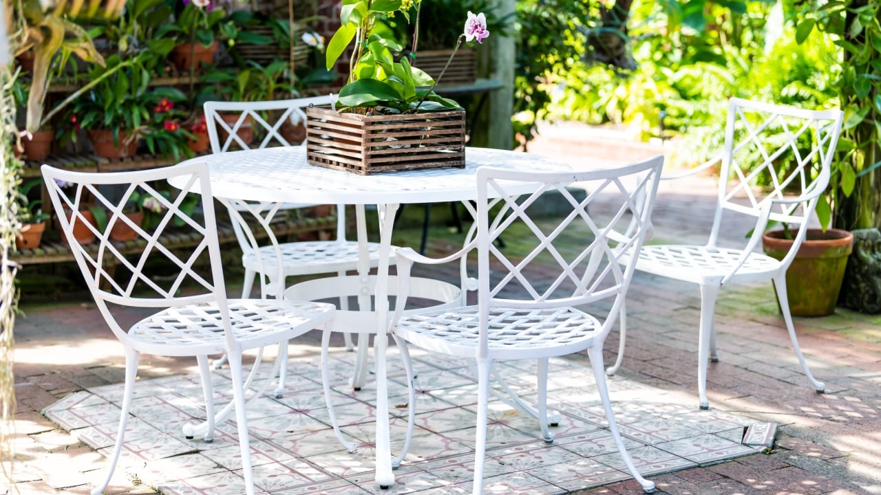 Four white cast iron chairs and table at outdoor or outside sitting garden or patio with potted orchid flowers, pots on sunny day