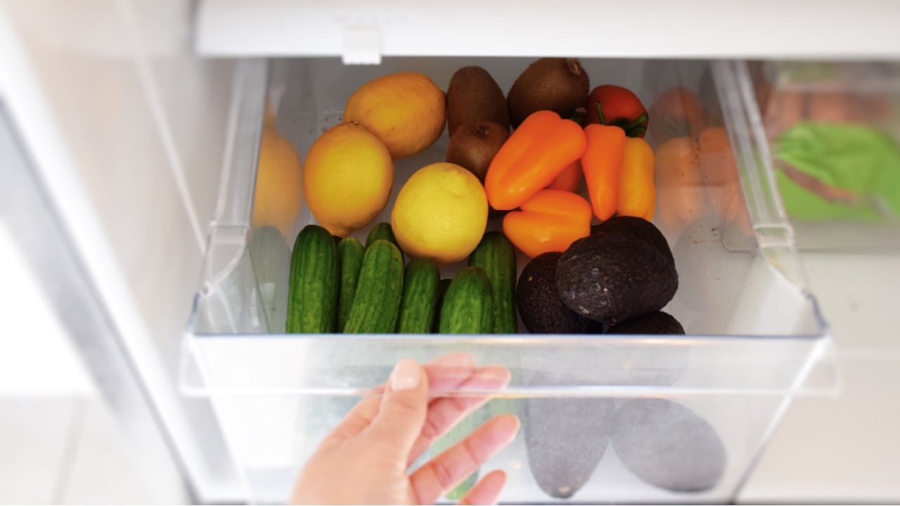 Female hand taking vegetables from a crisper drawer of a refrigerator