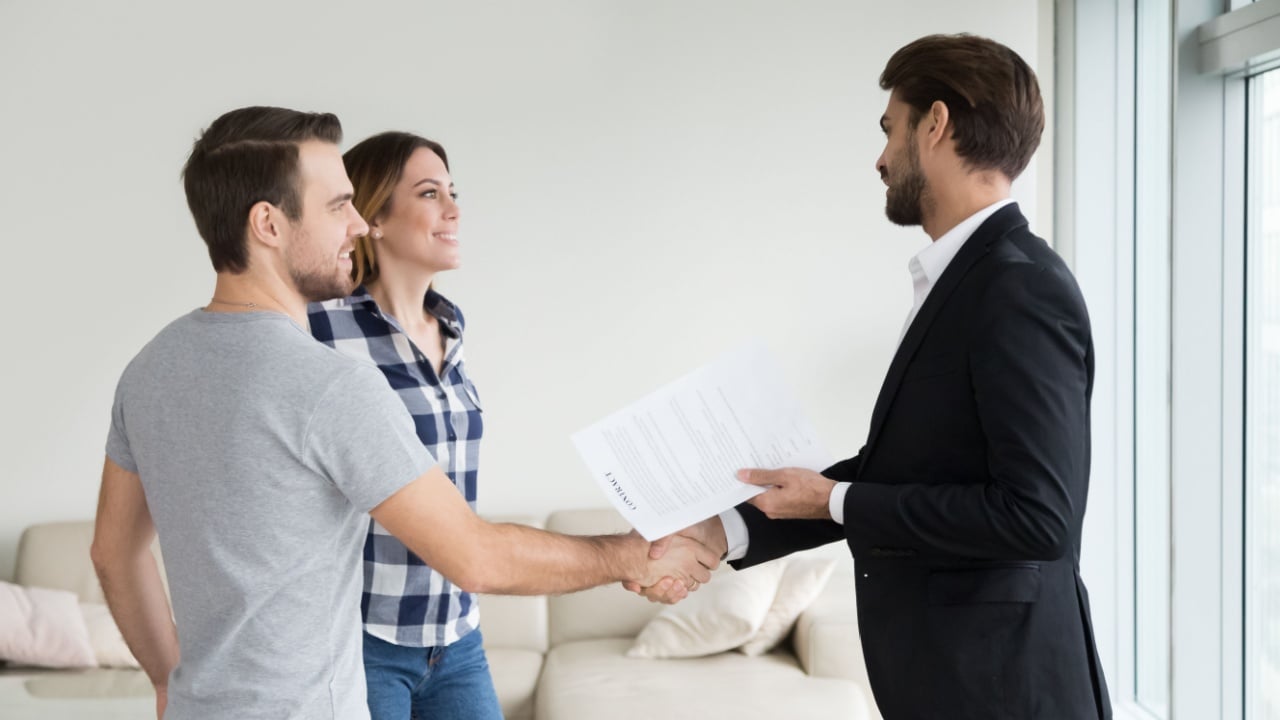 Realtor or landlord handshaking couple buyers tenants make real estate deal holding rental agreement or sale purchase contract, agent and clients shake hands welcoming renters in new home apartment