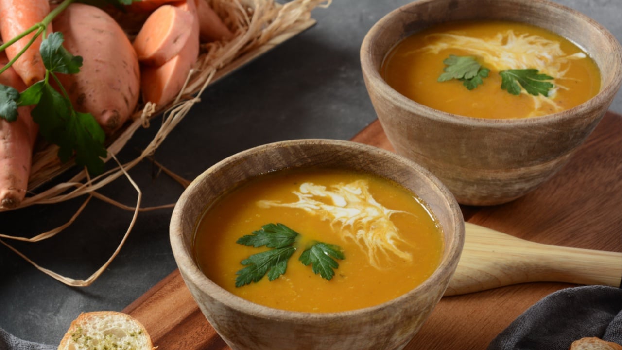 Sweet potato and carrot soup served with sour cream in wooden bowl. Orange vegetable soup.