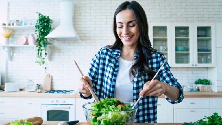 Beautiful young woman is preparing vegetable salad in the kitchen. Healthy Food. Vegan Salad. Diet. Dieting Concept. Healthy Lifestyle. Cooking At Home. Prepare Food. Cutting ingredients on table