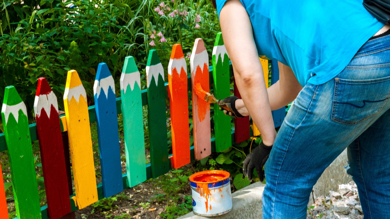 woman strokes the garden fence with colorfully paint in summer.