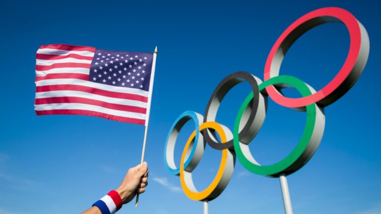 RIO DE JANEIRO - MARCH, 2016: A hand of a Team USA supporter wearing red white and blue sweatband holds an American flag in front of Olympic Rings.