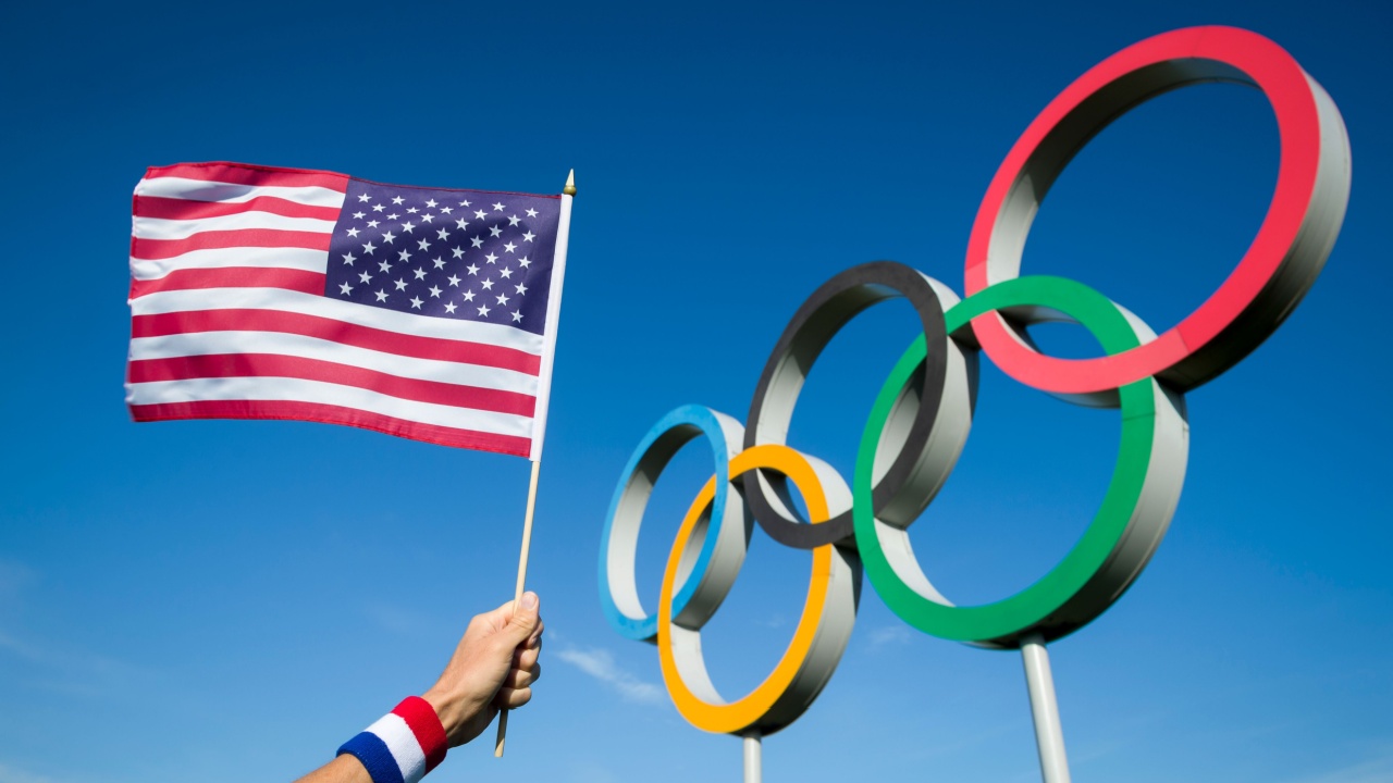 RIO DE JANEIRO - MARCH, 2016: A hand of a Team USA supporter wearing red white and blue sweatband holds an American flag in front of Olympic Rings.