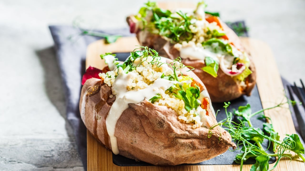 Baked sweet potatoes stuffed with quinoa, vegetables and tahini dressing, copy space. Baked vegetables, vegan food concept.
