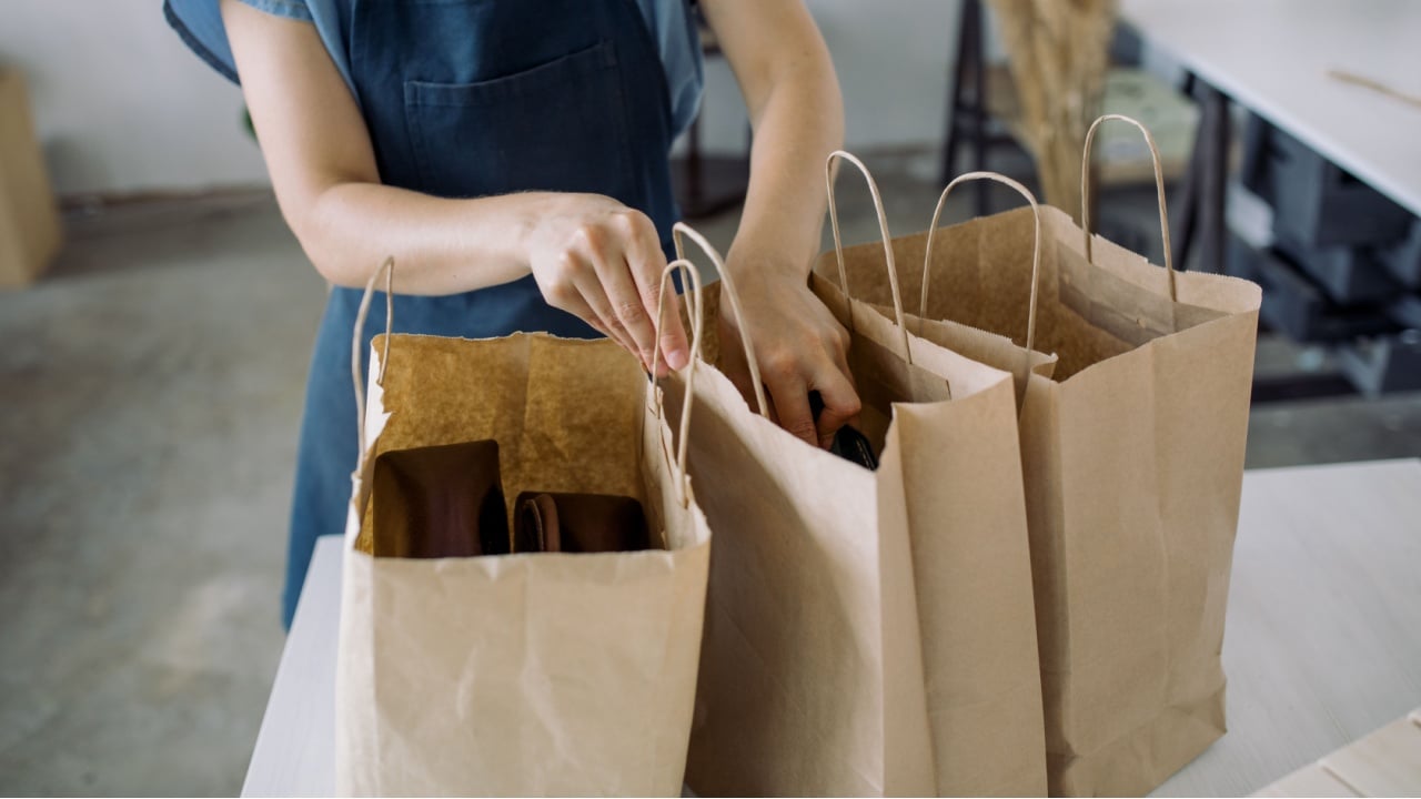 Row of paper bags. Woman in apron packing purchases into paper bags for home delivery. Small business concept. 