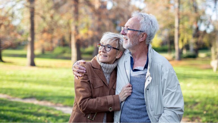 Mature couple walking thru public park on sunny day and smile