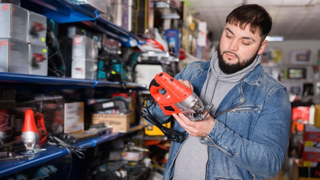 Glad cheerful smiling confident buyer chooses an electric tool in hardware store