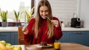 Cheerful young girl eating christmas cake while sitting at the kitchen