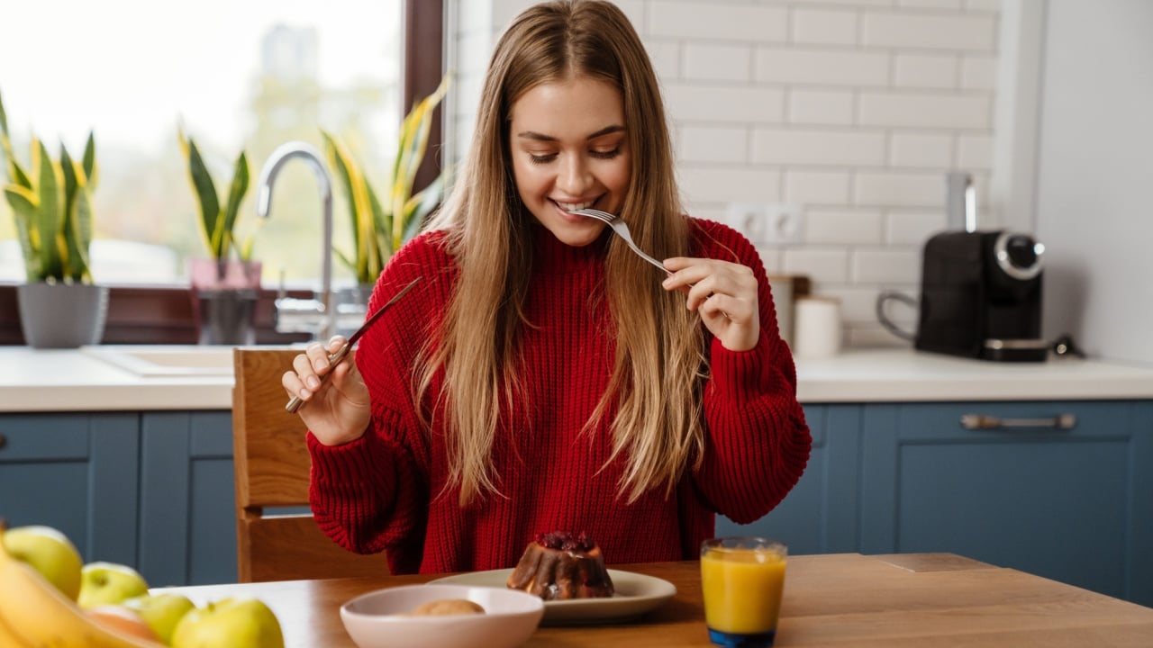 Cheerful young girl eating christmas cake while sitting at the kitchen