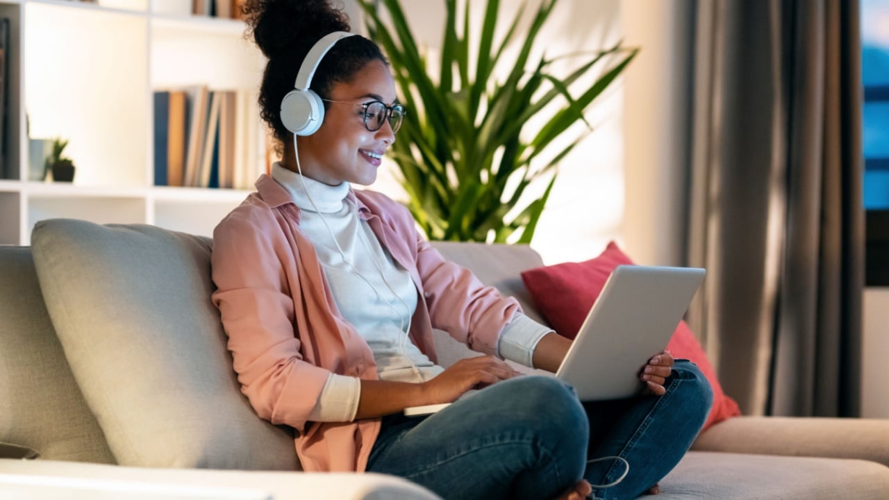 Shot of beautiful young entrepreneur woman working with laptop while listening music with headphones sitting on couch in the office.