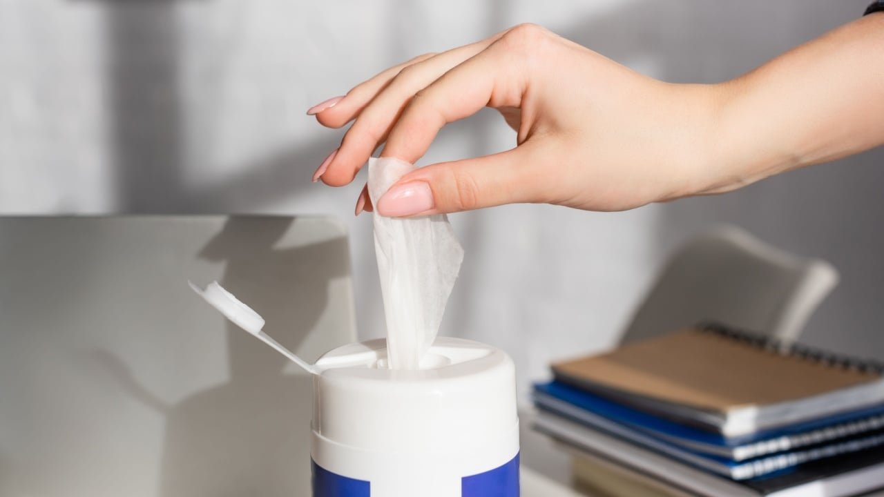 Cropped view of woman taking cleansing napkin near laptop and notebooks on blurred background