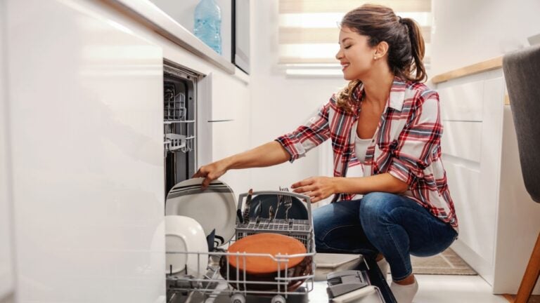 Diligent housewife putting dishes into dishwasher.