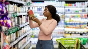 Pretty African American woman choosing groceries at supermarket, shopping for food, buying products for her family. Female consumer purchasing goods at huge mall, walking among shelves