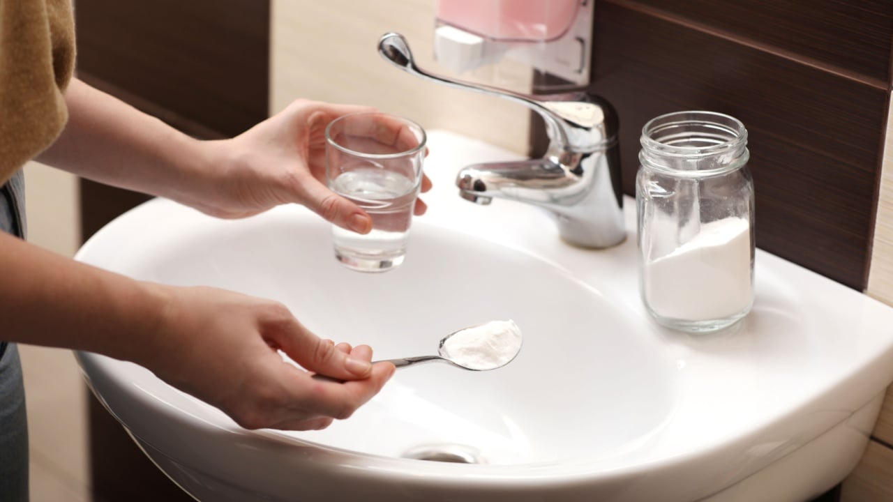 Woman using baking soda to unclog sink drain in bathroom,