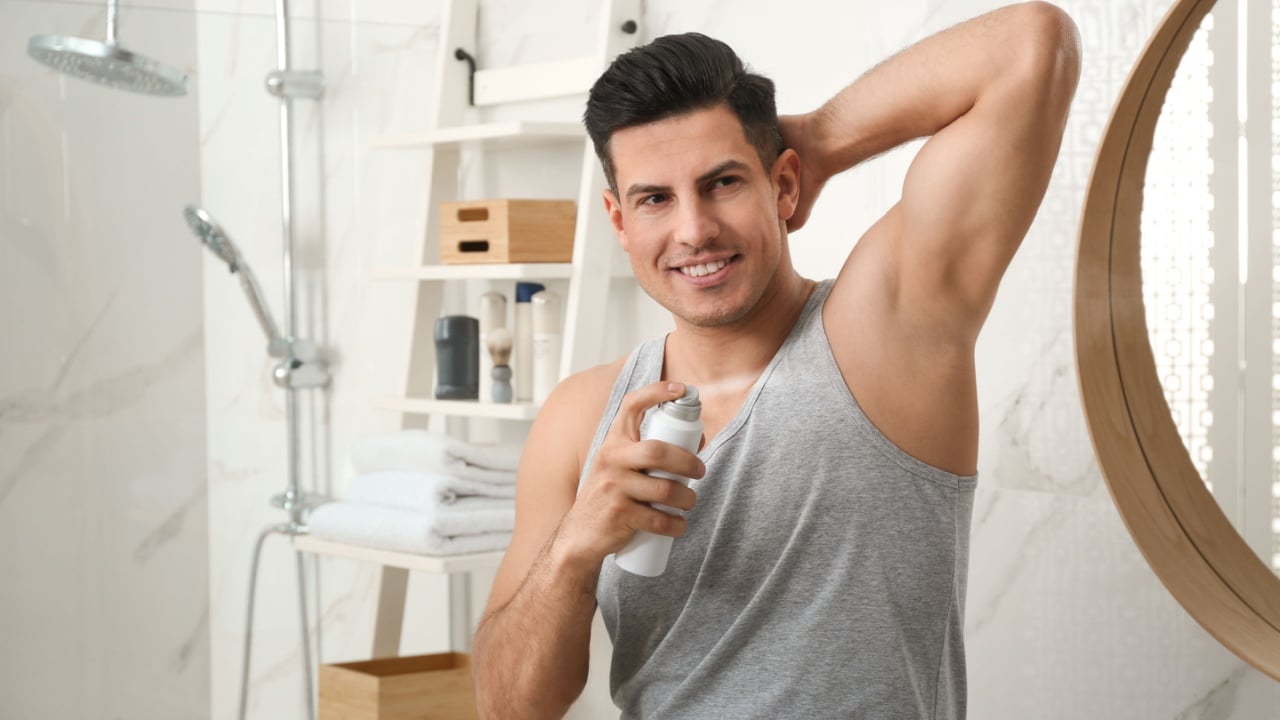Handsome man applying deodorant to armpit in bathroom, space for text