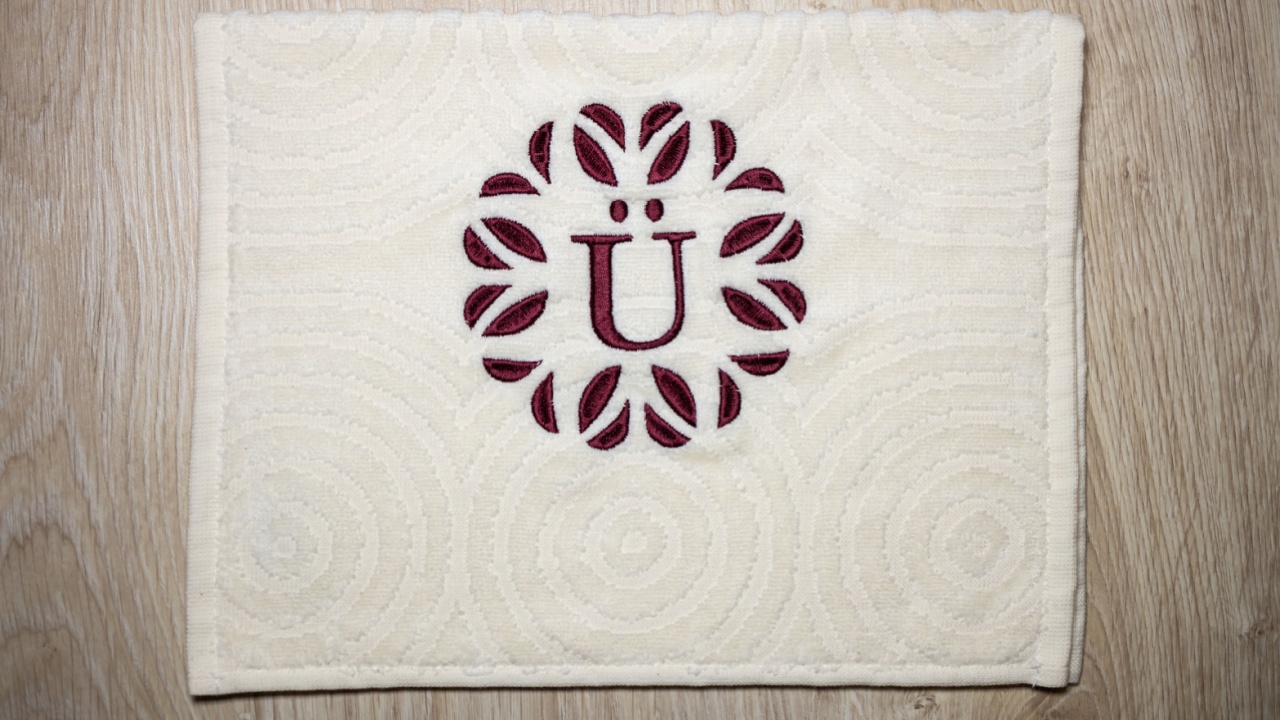 Embroidery design, alphabet monogram E and &Uuml;. Machine Embroidery on a cotton towel with burgundy color.