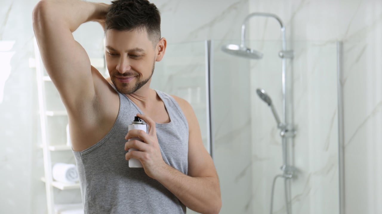 Handsome man applying deodorant in bathroom. Space for text