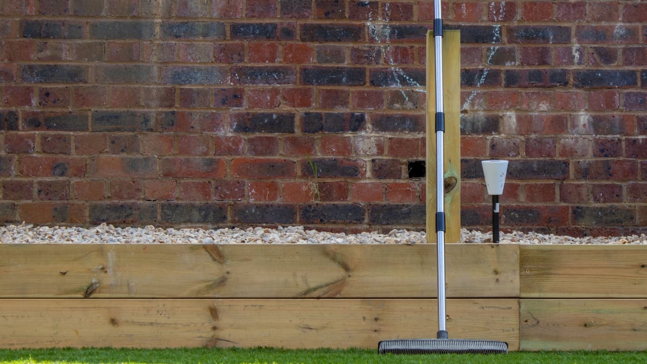 Rubber broom leaning on artificial grass in front of brick wall in a sunny urban garden
