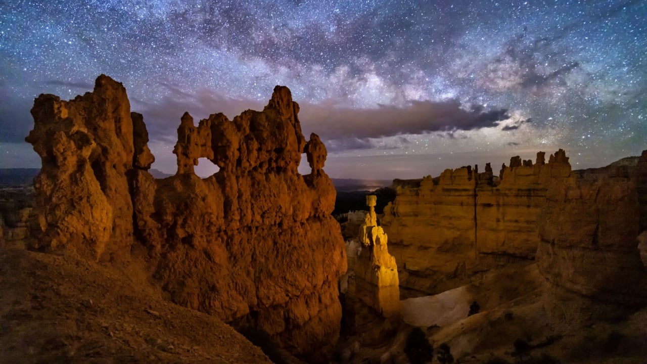 A hoodoo with small windows and Thor's Hammer against a night sky with clouds and the Milky Way below Sunset Point in ryce Canyon National Park, Utah.