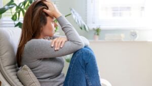 Stressed young woman looking away at window sitting on couch at home