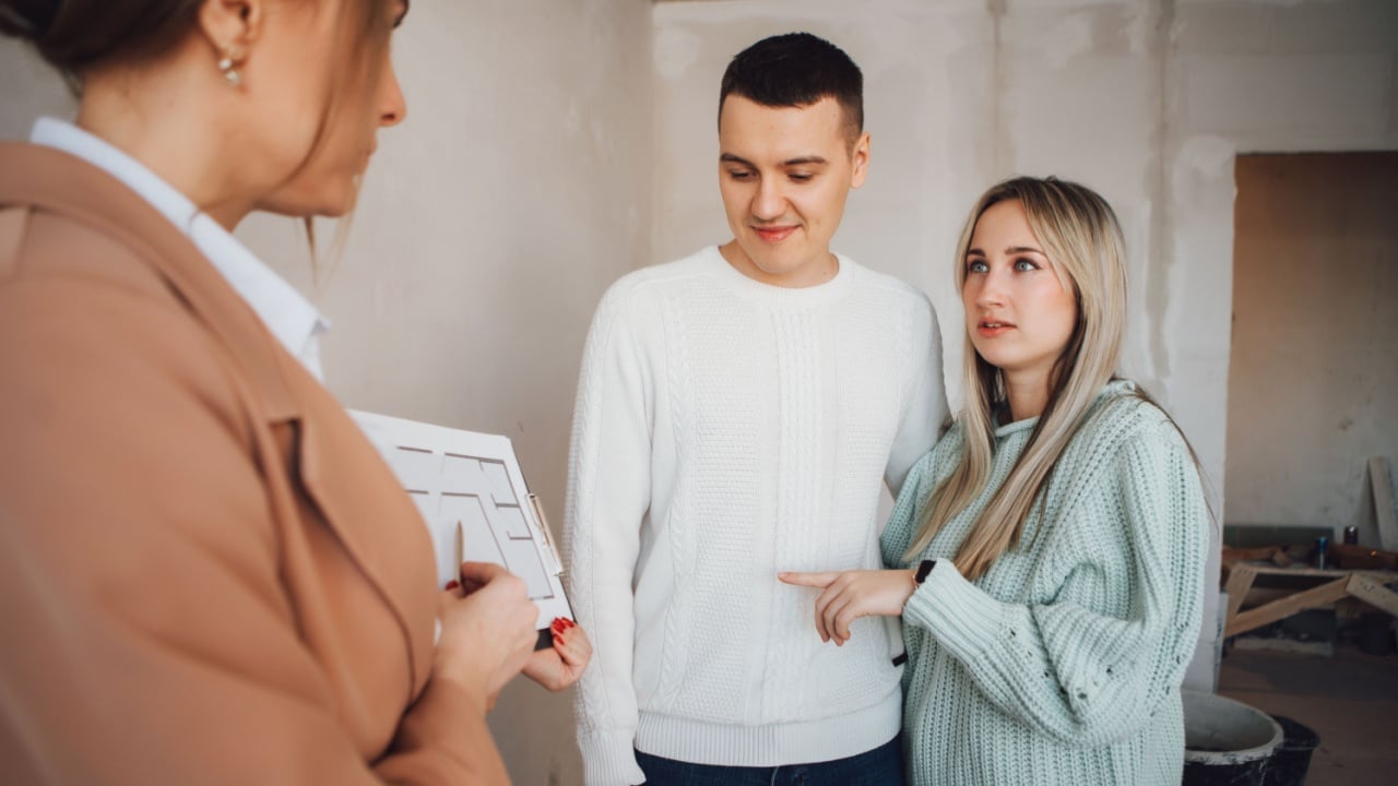 Real estate agent showing condo for sale to young couple. Female designer or realtor show apartment plan