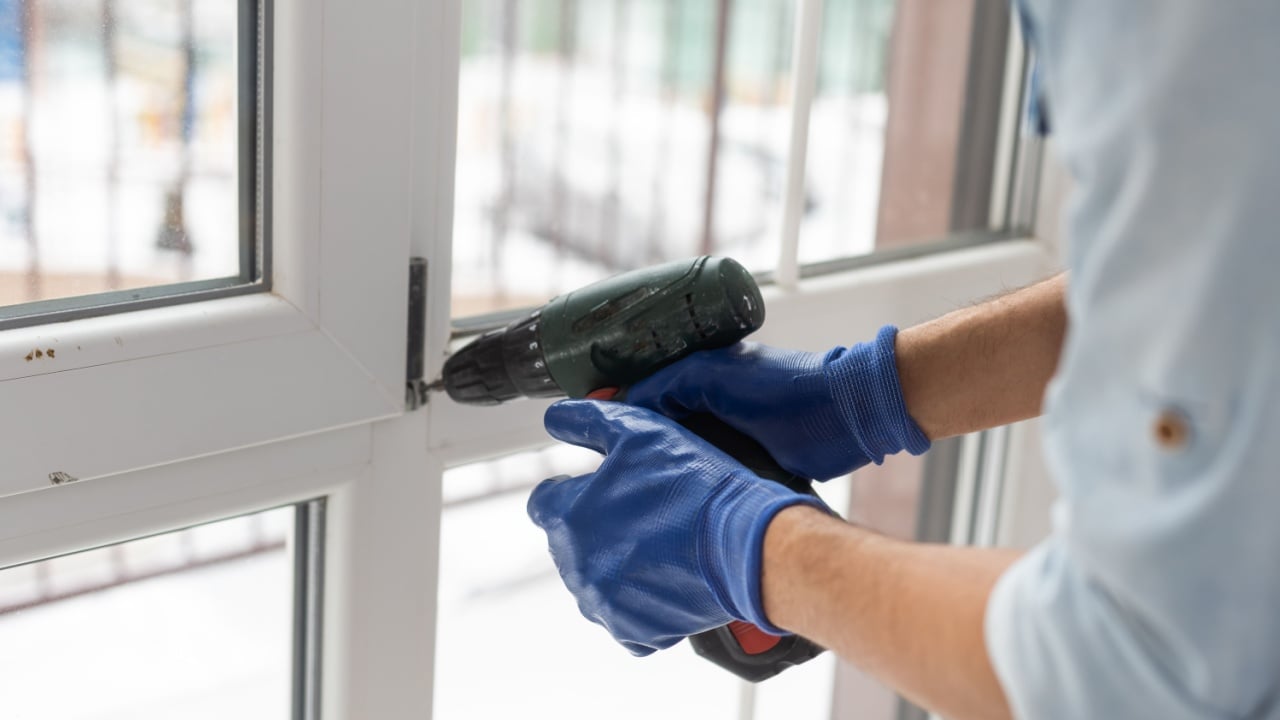 Man fixing lock to window with electric screwdriver